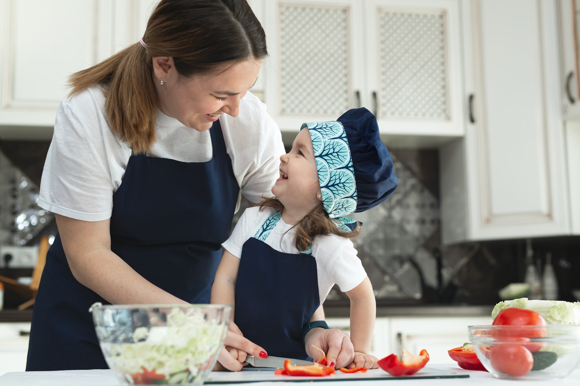 Caring mother teaches her little daughter how to prepare a salad in the kitchen, a young mother and