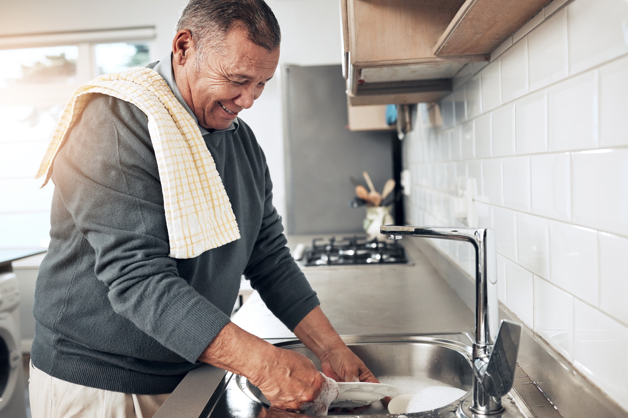 Cleaning, washing dishes or happy old man with soap and water in the kitchen sink in healthy home.