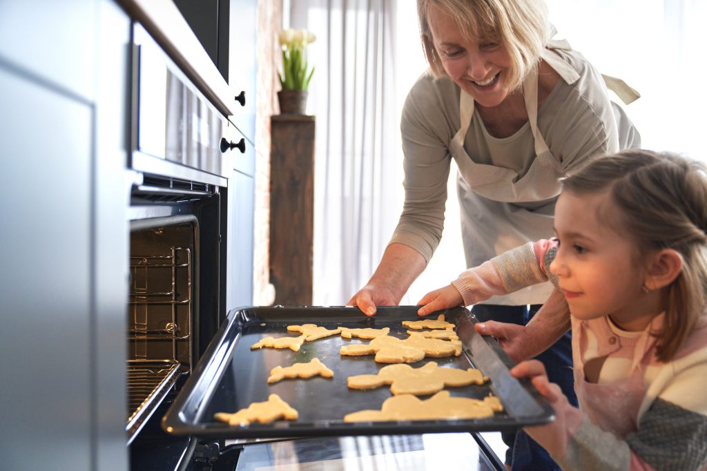 Happy grandma with granddaughter putting Easter cookies in the oven