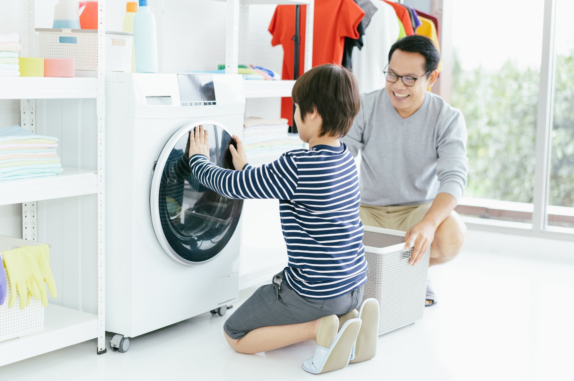 Happy smiling Asian family father and son in the laundry load a washing machine. Family activity.