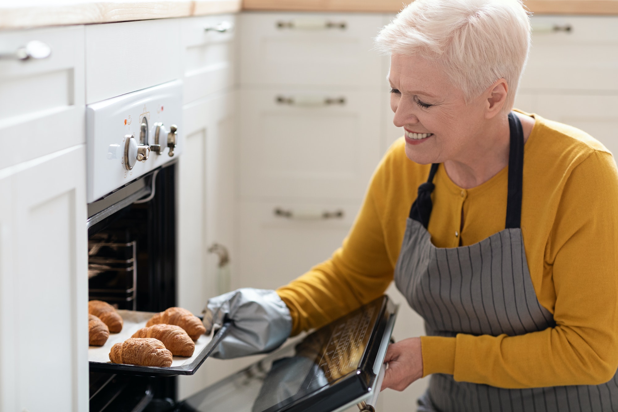 Smiling elderly woman taking croissants out of oven