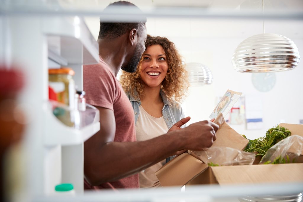 View Looking Out From Inside Of Refrigerator As Couple Unpack Online Home Food Delivery