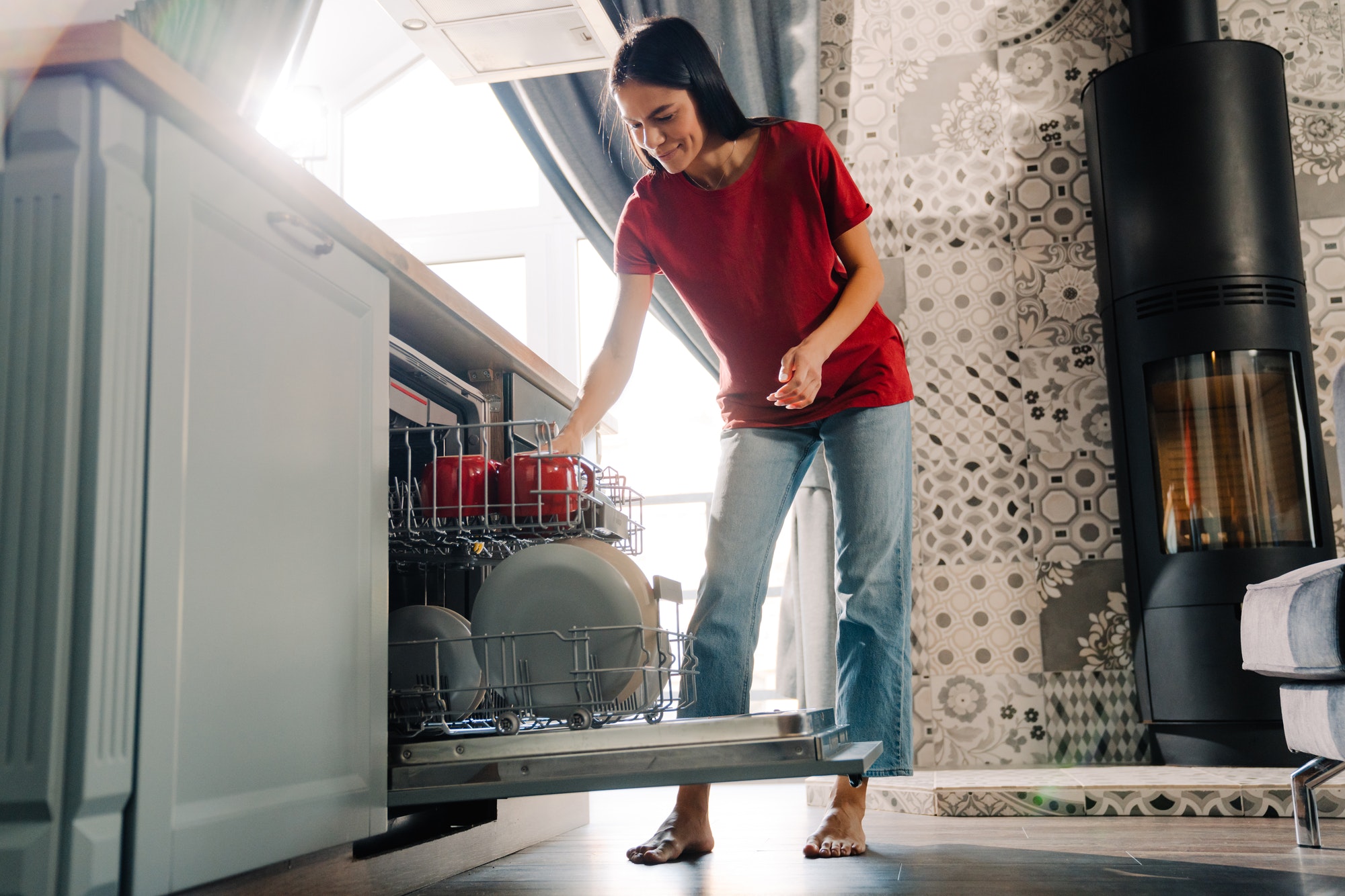 Young hispanic woman using dishwasher while doing housework