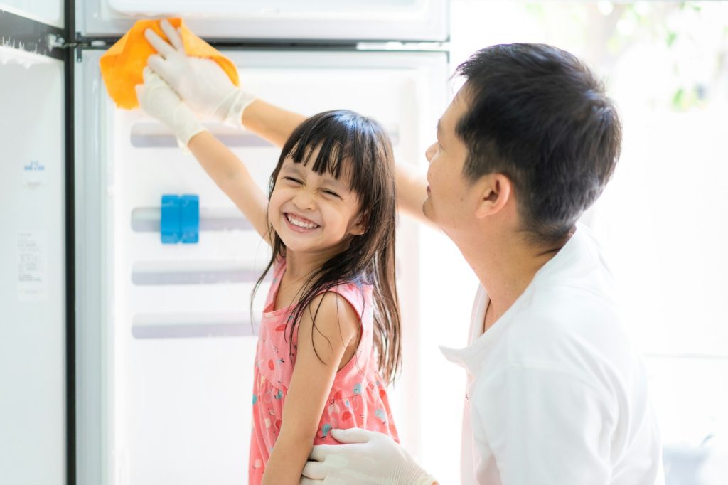 Asian daughter is helping father to clean the refrigerator with fully happiness moment.