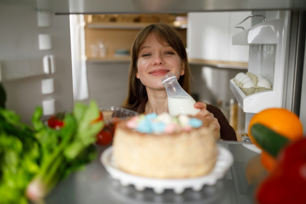 View from inside the refrigerator on a cheerful girl with a bottle of milk