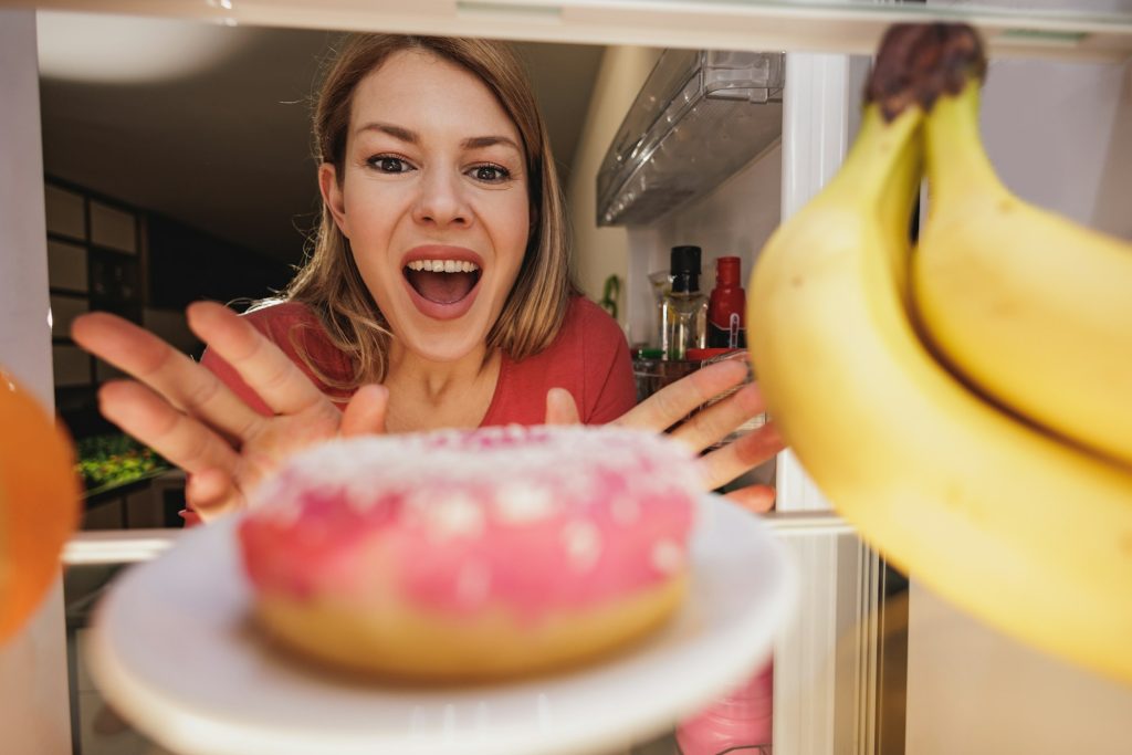 Woman Looking At Donut In Refrigerator